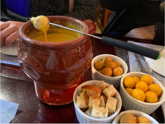 Fondue de queijo servido com pão e acompanhamentos